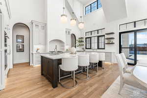 Kitchen featuring a breakfast bar, dual tone cabinetry, an island with sink, glass fronted cabinets, and pendant lighting