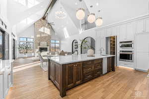 Two tone kitchen with two tone color scheme, a ceiling fan, a stone fireplace, light wood-style floors, and light stone counters