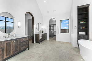 Bathroom featuring a freestanding tub, two vanities, lofted ceiling, and a spacious closet