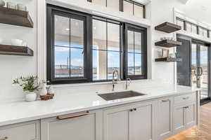 Kitchen featuring open shelves, light stone counters, light wood-type flooring, and gray cabinets
