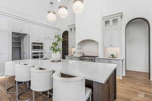 Dual tone kitchen featuring a kitchen bar, arched walkways, light stone countertops, a center island with sink, and two tone cabinets