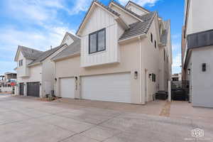 View of front facade featuring a gate, driveway, board and batten siding, and stucco siding