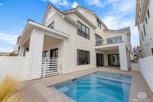 Back of house with stucco siding, a patio area, a balcony, and a pool with connected hot tub