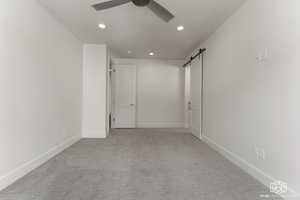 Spare room with a barn door, light colored carpet, ceiling fan, and recessed lighting