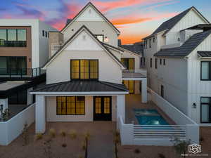 Back of property at dusk with a balcony, a standing seam roof, board and batten siding, a patio area, and stucco siding