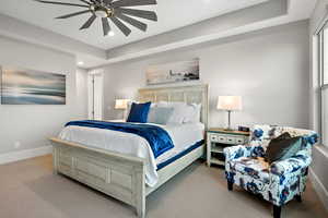 Carpeted bedroom with a ceiling fan and a tray ceiling