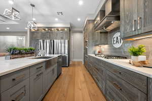 Kitchen with light wood finished floors, decorative light fixtures, stainless steel appliances, light stone countertops, and glass fronted cabinets