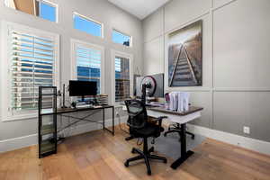 Home office featuring light wood-style floors, a high ceiling, and a decorative wall