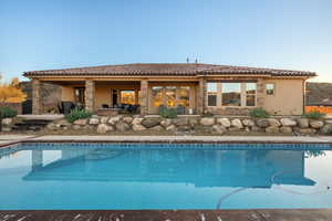 Rear view of property featuring a patio area, stucco siding, a tiled roof, and stone siding