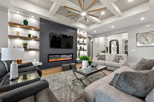 Living room with built in features, wood finished floors, a glass covered fireplace, coffered ceiling, and recessed lighting