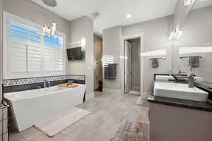 Bathroom featuring a soaking tub, double vanity, walk in shower, and suspended lighting