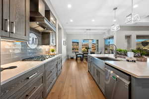 Kitchen with light stone countertops, gray cabinets, stainless steel appliances, pendant lighting, and light wood-type flooring
