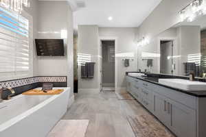 Full bath featuring double vanity, a soaking tub, and hanging lights