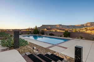 Pool at dusk with a fenced backyard and a patio