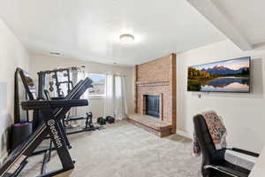 Exercise area featuring a fireplace, carpet flooring, and a textured ceiling