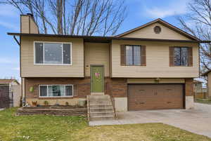 Raised ranch featuring brick siding, a garage, driveway, a chimney, and a front lawn