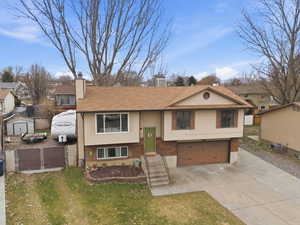 Bi-level home with an attached garage, brick siding, concrete driveway, a chimney, and a residential view