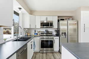Kitchen featuring stainless steel appliances, dark countertops, white cabinetry, and light wood finished floors