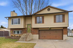 Raised ranch with brick siding, a garage, and concrete driveway