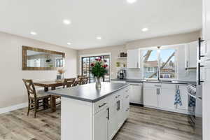 Kitchen featuring dark countertops, stainless steel appliances, white cabinetry, open shelves, and light wood finished floors