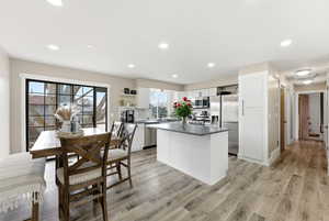 Kitchen with white cabinetry, a kitchen island, stainless steel appliances, dark countertops, and light wood-style floors