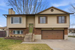 Split foyer home with brick siding, an attached garage, concrete driveway, and a chimney