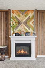 Detailed view of a glass covered fireplace, wooden walls, and a textured ceiling