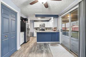 Kitchen featuring stainless steel appliances, white cabinets, a ceiling fan, light wood finished floors, and a textured ceiling
