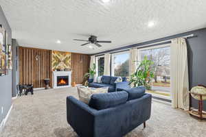 Living area with light carpet, a textured ceiling, a lit fireplace, ceiling fan, and wooden walls