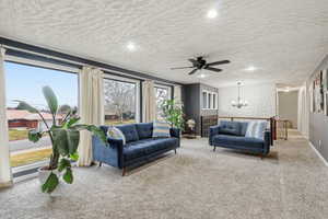 Living room with carpet floors, a ceiling fan, suspended lighting, and a textured ceiling