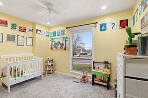 Bedroom featuring a crib, carpet flooring, a ceiling fan, recessed lighting, and a textured ceiling