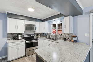 Kitchen with a textured ceiling, stainless steel appliances, white cabinets, decorative backsplash, and light wood finished floors