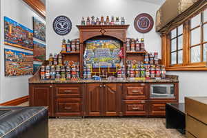 Indoor wet bar with open shelves, stainless steel microwave, dark stone counters, and bold wood finish cabinetry