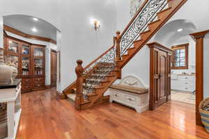 Staircase featuring arched walkways, hardwood / wood-style flooring, a high ceiling, recessed lighting, and ornamental molding