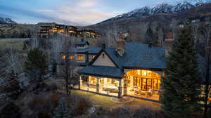 Back of house at dusk with a mountain view, a chimney, a patio, and a high end roof