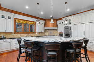 Kitchen with glass fronted cabinets, a breakfast bar, stainless steel appliances, crown molding, and pendant lighting