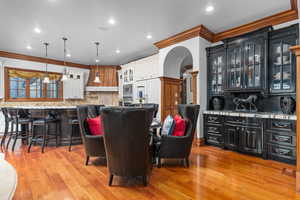 Dining space with ornamental molding, arched walkways, light wood-style flooring, and recessed lighting