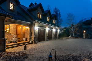 House at twilight with a porch, decorative driveway, a garage, and brick siding