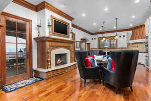 Living area featuring crown molding, a fireplace, light wood finished floors, recessed lighting, and arched walkways