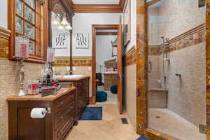 Ensuite bathroom with ornamental molding, vanity, a stall shower, and wainscoting