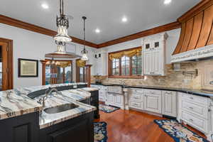 Dual tone kitchen featuring two tone cabinetry, dark stone counters, glass fronted cabinets, ornamental molding, and dark wood-style flooring