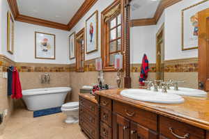 Full bath featuring wainscoting, tile walls, crown molding, vanity, and a freestanding bath