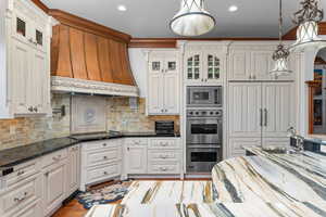 Kitchen featuring glass fronted cabinets, stainless steel appliances, dark stone countertops, and decorative light fixtures