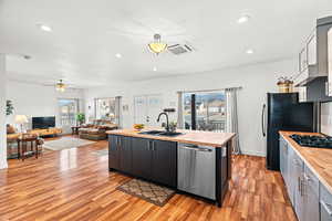 Kitchen featuring a center island with sink, black appliances, open floor plan, wooden counters, and light wood finished floors