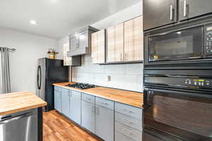 Kitchen with black appliances, gray cabinetry, butcher block countertops, backsplash, and light wood finished floors
