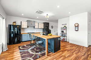 Kitchen with butcher block counters, black appliances, a kitchen island with sink, cooling unit, and tasteful backsplash