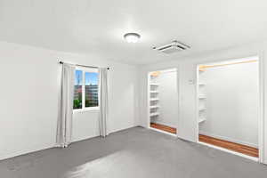 Unfurnished bedroom with cooling unit, concrete flooring, and multiple closets