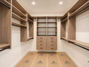 Primary Custom closet system featuring natural wood-finish shelving, integrated drawers with dark hardware, and multiple hanging rods