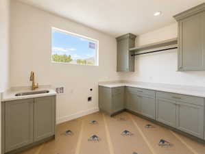Utility room featuring extensive cabinetry in a muted green finish, light-toned countertops, and a stainless steel sink with a gold-tone faucet