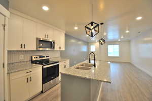 Kitchen featuring stainless steel appliances, an island with sink, light wood finished floors, light stone counters, and pendant lighting